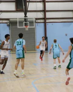 A basketball game in an indoor court, featuring players in blue and white uniforms dribbling a ball and preparing for a play