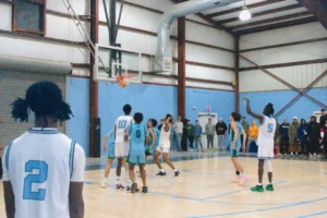 A basketball game in progress, with players wearing blue and white jerseys aiming for the basket, surrounded by an audience
