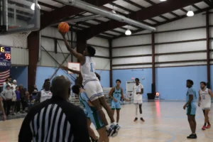 A basketball player jumps for a layup during a game, while referees and teammates observe in a gymnasium setting
