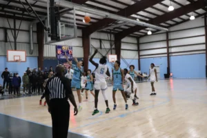 A basketball player shoots a free throw amid a competitive game, with spectators watching and the score displayed above
