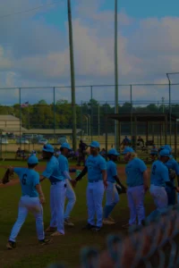 A group of baseball players in light blue uniforms engage in a high-energy group interaction on a field with distant spectators