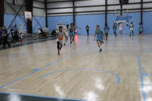 A young basketball player dribbles a ball towards the hoop while opposing players sprint after him on a gymnasium's wooden court